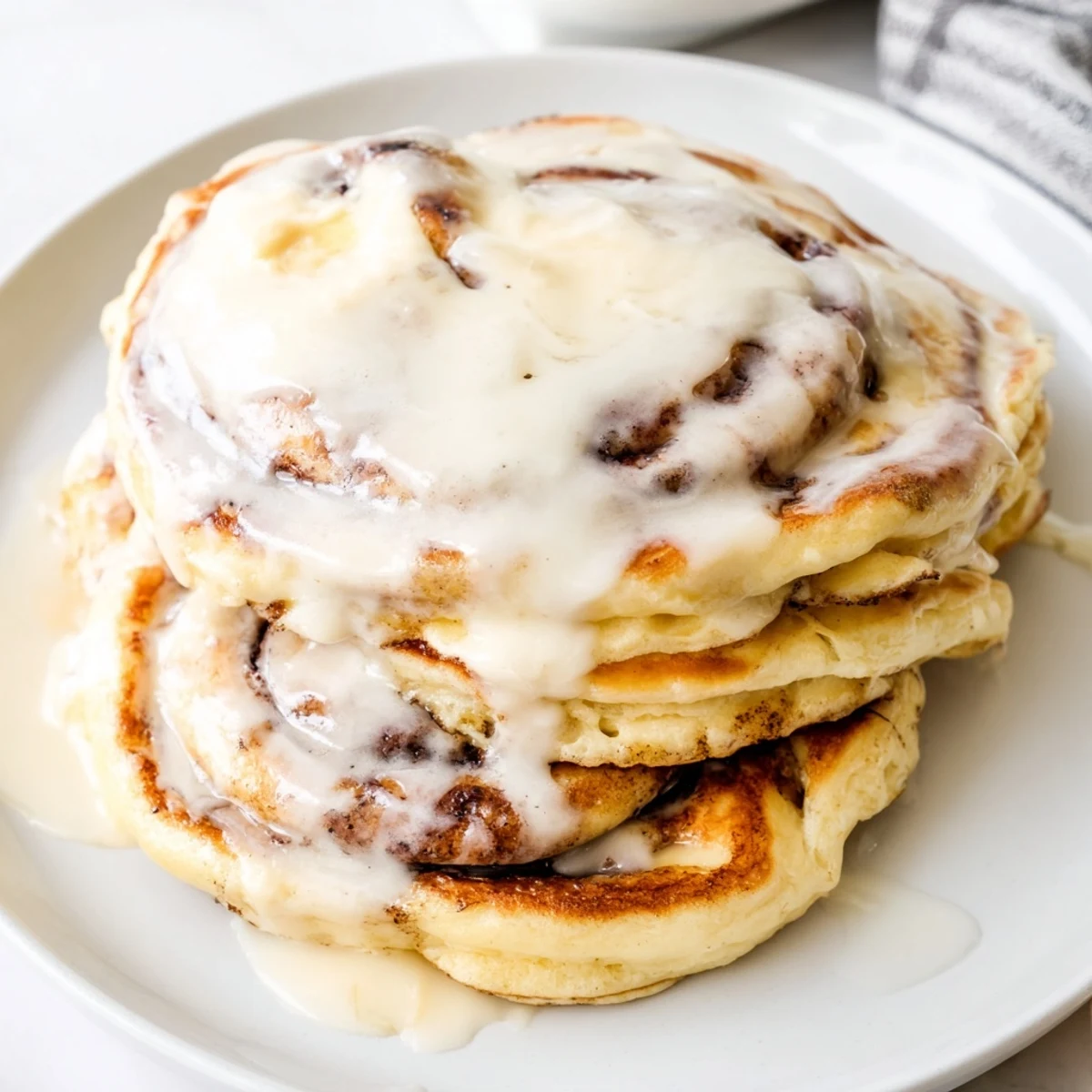 Golden brown Cinnamon Roll Pancakes drizzled with sweet cream cheese frosting, a delightful breakfast.