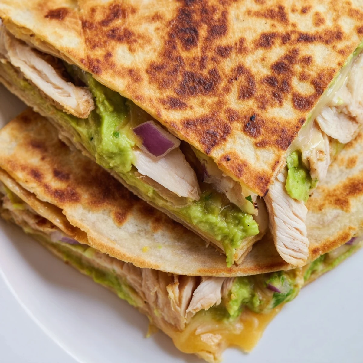 Golden-brown Chicken Avocado Quesadilla wedges filled with melted cheese and creamy avocado mash on a plate.