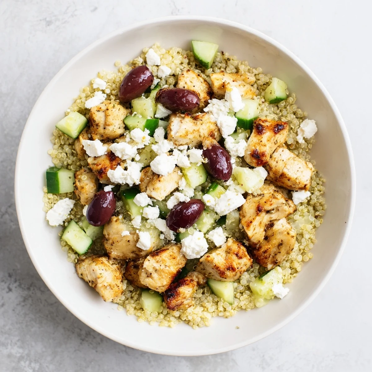 A vibrant Mediterranean Chicken Bowl with golden chicken, chickpeas, olives, feta, cucumber, tomatoes, red onion, and fluffy quinoa, drizzled with zesty lemon-oregano dressing.