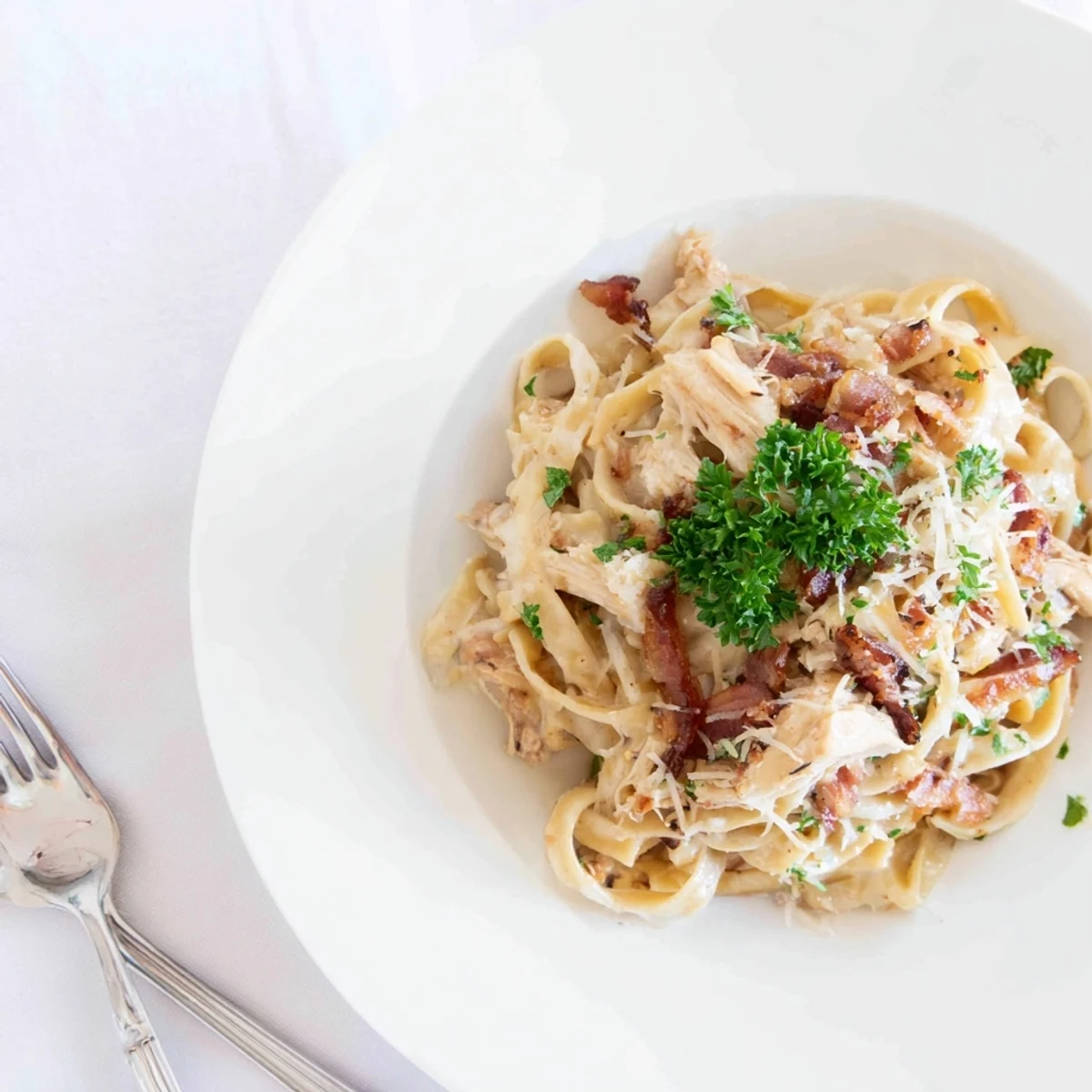Steaming plate of Chicken Carbonara topped with fresh parsley, featuring tender bacon and shredded chicken in velvety sauce.