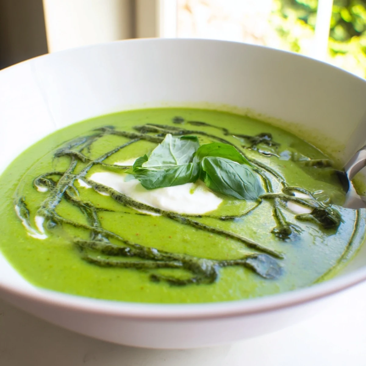 A close-up of Courgette, Pea and Pesto Soup with a dollop of Greek yogurt and fresh basil leaves on top.