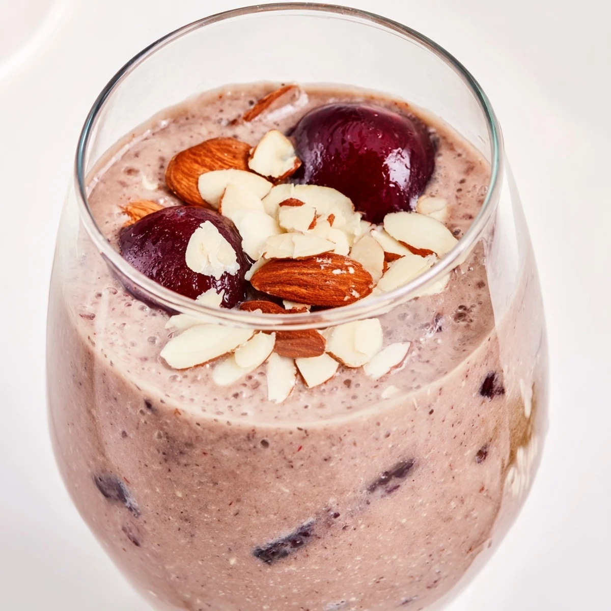 Thick and frothy Cherry Almond Smoothie swirled with almond butter, poured into a rustic glass against a bright kitchen backdrop.