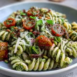 Colorful bowl of al dente pasta tossed in basil pesto, cherry tomatoes, and arugula for a fresh, flavorful dish.  