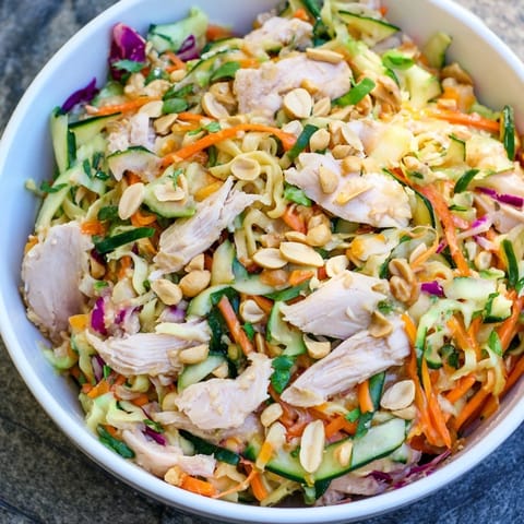 Enjoy a bowl of refreshing Thai-Inspired Peanut Chicken Pasta, complete with peanuts and colorful bell peppers.