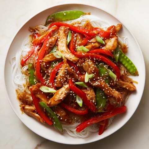 Golden brown Mongolian Chicken with glistening sauce, served on a bed of fluffy rice noodles.