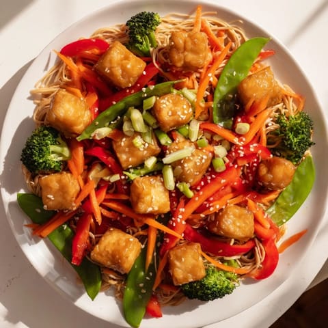 A steaming bowl of Sesame Ginger Tofu Stir-Fry with tender noodles and a glossy, flavorful sauce.