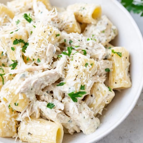 A close-up of a bubbling Slow Cooker Chicken Alfredo Pasta Bake, garnished with fresh parsley and cheese.