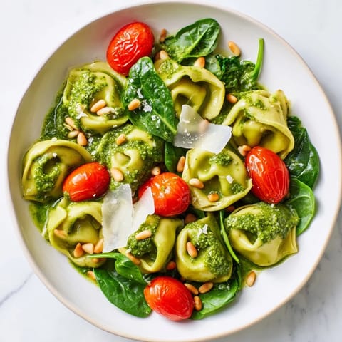 Chilled Pesto Tortellini Salad served in a rustic bowl, featuring vibrant green pesto and grated Parmesan garnish.