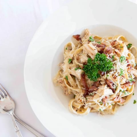 Steaming plate of Chicken Carbonara topped with fresh parsley, featuring tender bacon and shredded chicken in velvety sauce.