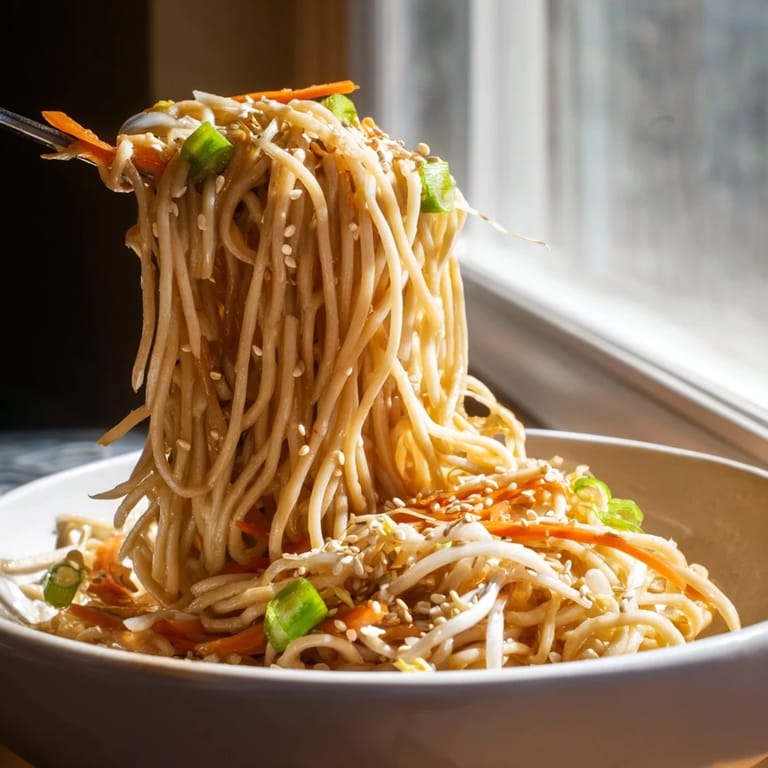 Tossed noodles in a rich garlic-butter sauce, garnished with red chili slices and fresh cilantro leaves.