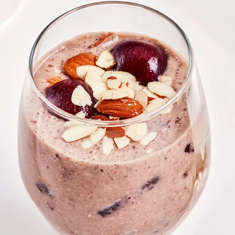 Thick and frothy Cherry Almond Smoothie swirled with almond butter, poured into a rustic glass against a bright kitchen backdrop.