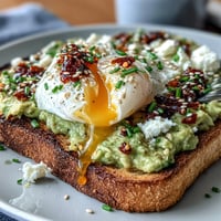 Creamy avocado spread on golden sourdough toast, topped with a perfectly poached egg and a spicy chili crisp drizzle for a vibrant breakfast.